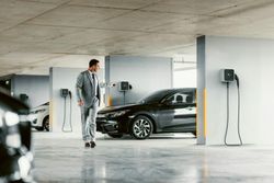 Homme quittant son véhicule électrique branché sur une borne de recharge à domicile