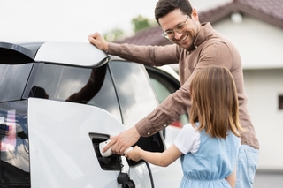 A man and his daughter charge an electric car at home