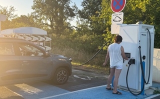 Femme utilisant une borne de recharge pour recharger sa voiture électrique, illustrant les technologies intelligentes et confort de vie.